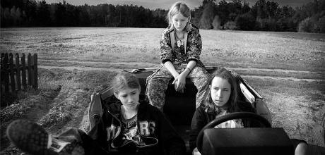 Trzy dziewczynki siedzące w aucie, za nimi widać pole i las